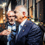 Two men in suits embrace amid orange confetti on a city street, with security in the background.
