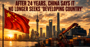 Red Chinese flag waves over Shanghai skyline at sunset, with shipping containers and a crane in the foreground and a bold news headline about China no longer seeking ‘developing country’ status.