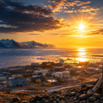 Arctic sunset over Utqiagvik, Alaska, with snow-lined town and distant mountains across icy water, sign in foreground.