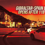Banner announcing the Gibraltar–Spain border opens after 118 years over a rocky hill with a street and parked cars, sunset colors in the background, conveying news.
