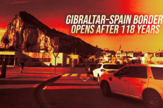 Banner announcing the Gibraltar–Spain border opens after 118 years over a rocky hill with a street and parked cars, sunset colors in the background, conveying news.